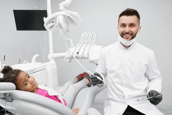 Alegre dentista masculino sonriendo mientras trabaja y cura los dientes —  Fotos de Stock