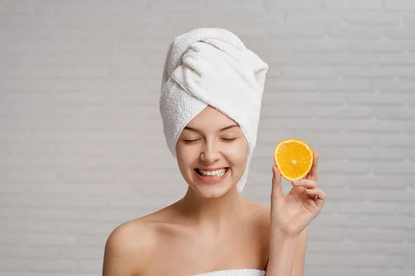 Mujer joven con toalla en la cabeza manteniendo la naranja fresca en la mano —  Fotos de Stock