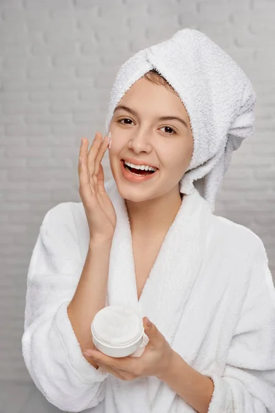Retrato de mujer feliz en toalla aplicando cara de crema —  Fotos de Stock