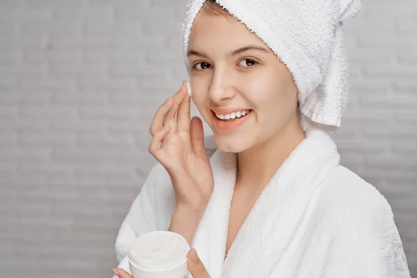 Cheerful lady in dressing gown applying cream on soft skin — Stock Photo, Image