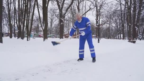 Senior cleaner removing snow with broom. — Stock Video