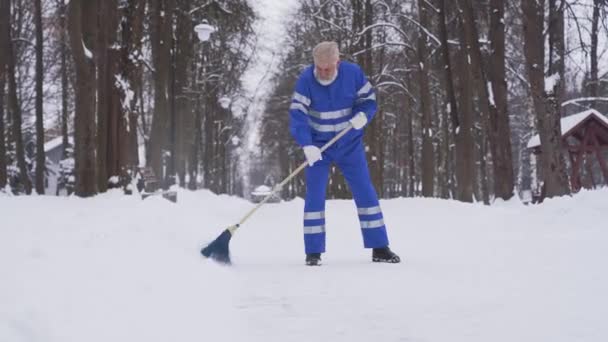 Senior cleaner removing snow with broom. — Stock Video