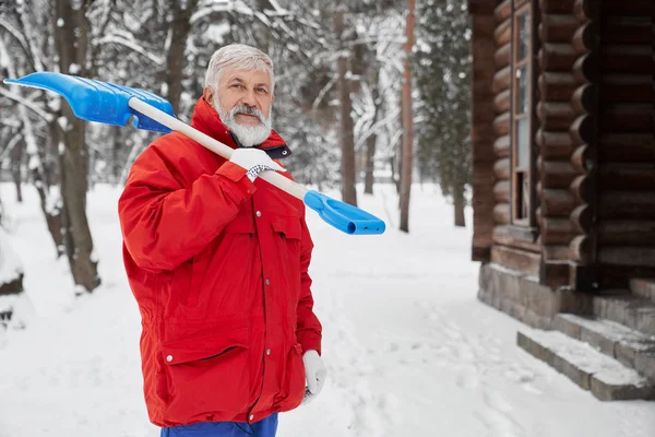 Grandfather keeping shovel in shoulder and smiling in winter