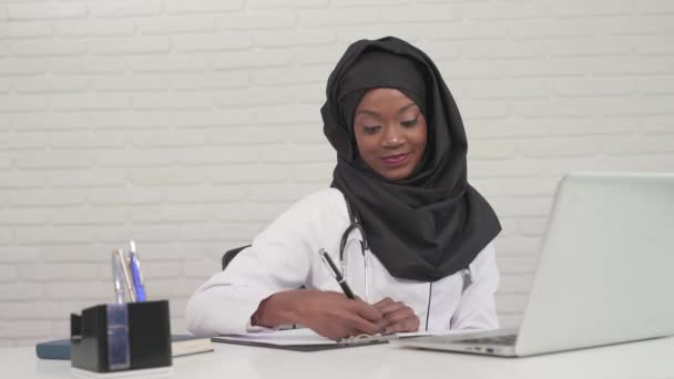 Female doctor writing notes and typing on laptop. — Stock Video