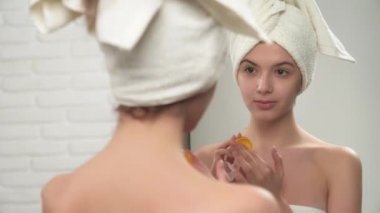 Woman in towels putting balm on lips.