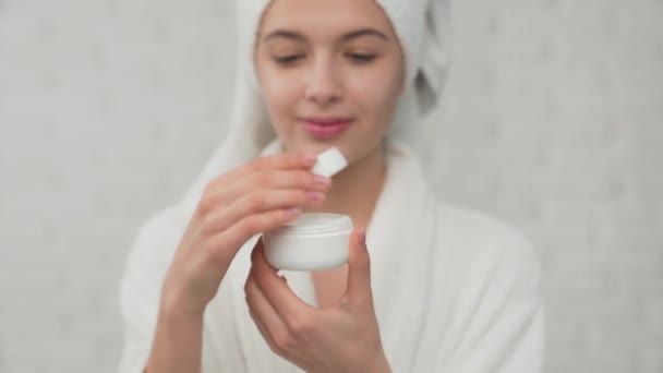 Woman in towel putting cream on face. — Stock Video