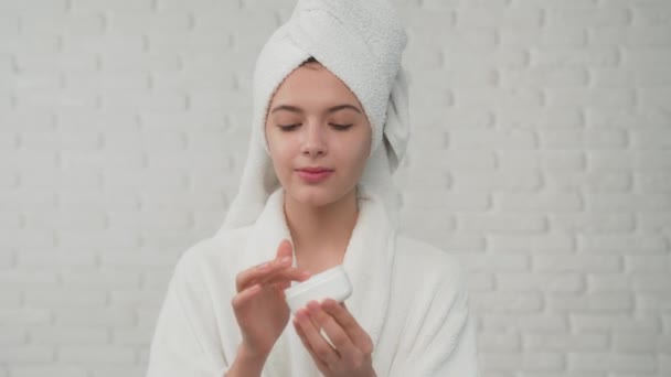 Woman in bathrobe putting cream on face. — Stock Video