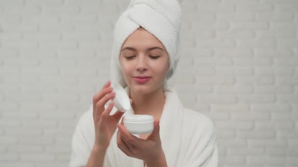 Mujer en albornoz poniendo crema en la cara . — Vídeo de stock