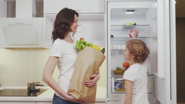 Woman and her daughter putting eco food into refrigerator — Stock Video