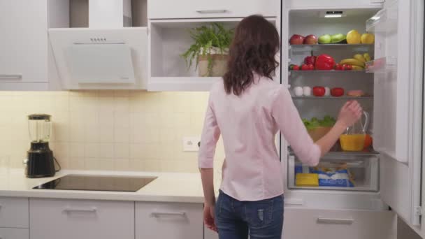Jovem mãe tomando suco de laranja da geladeira para a filha — Vídeo de Stock