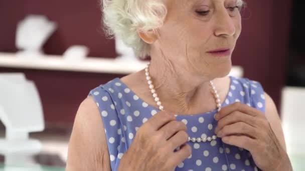 Очаровательная пожилая леди примеряет жемчужное ожерелье в ювелирном магазине — стоковое видео