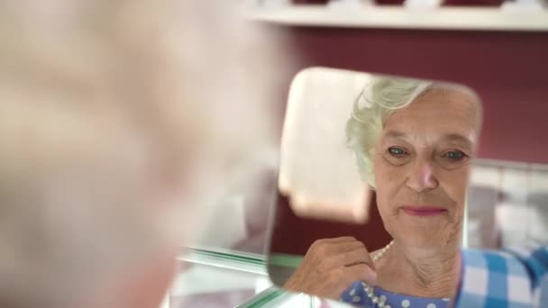 Зрелая леди смотрит в зеркало, примеряя жемчужное ожерелье — стоковое видео