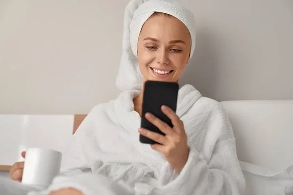 Усміхнена дівчина використовує смартфон у ліжку . — стокове фото