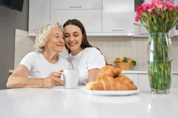 Jong meisje knuffelen grootmoeder in keuken. — Stockfoto