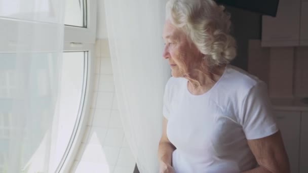 Oudere vrouw helaas kijkend door het raam. — Stockvideo