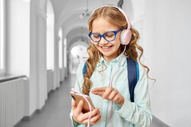 Elinde telefon tutan ve müzik dinleyen liseli kız..