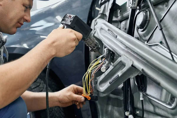 Side view of car electric using soldering iron to blend wire — ストック写真