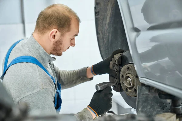 Mechanic checking serviceability of brake pads in lifted car — ストック写真