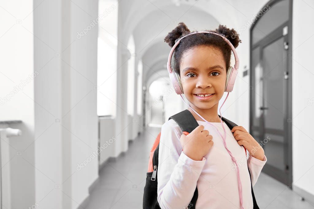 African school girl wearing headphones standing at corridor.