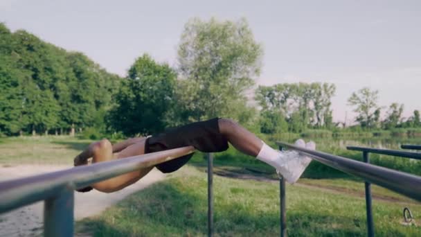 Stark idrottsman gör sit ups i grön park på parallella barer — Stockvideo