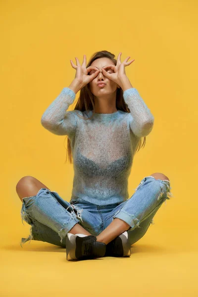 Смішна дівчина сидить з натиснутими губами, показуючи окуляри пальцями — стокове фото