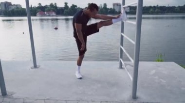Full length portrait of african guy stretching leg near lake