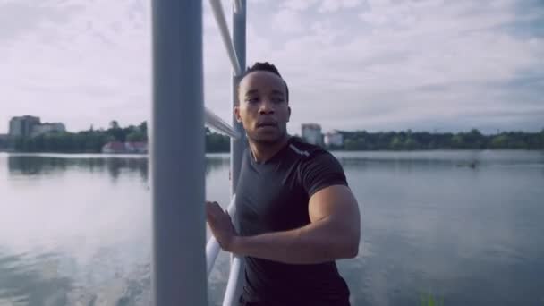 Afro uomo allungamento delle braccia dopo l'allenamento serale vicino al lago — Video Stock