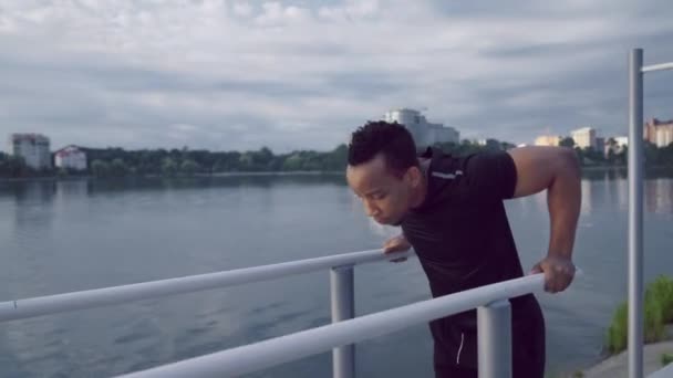 Afro homme faire triceps trempettes sur barres parallèles près du lac — Video