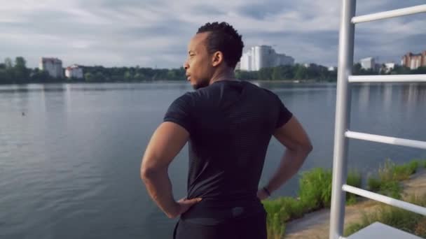Musclé afro-américain homme en vêtements de sport regardant le lac — Video