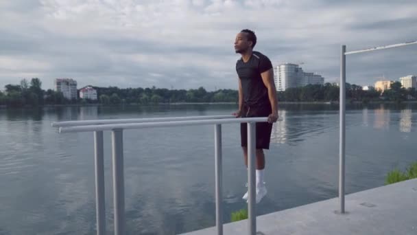 Silný africký chlap dělá push up na paralelní tyče v blízkosti jezera — Stock video