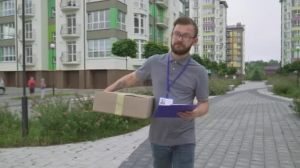 Kurir memeriksa alamat di papan klip dan membawa paket — Stok Video