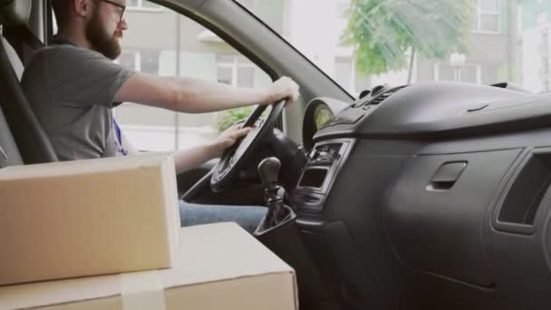 Young delivery man driving car with parcels on front seat — Stok video