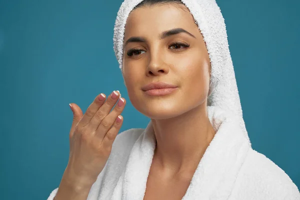 Woman in bathrobe applying cream on face. — Stock Photo, Image