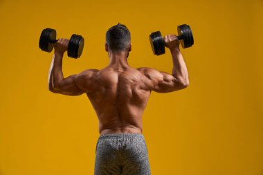 Güçlü atletik adam dambıllarla egzersiz yapıyor.