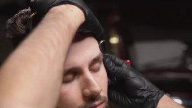 Sakallı adam berber dükkanında kaşlarını düzeltiyor.