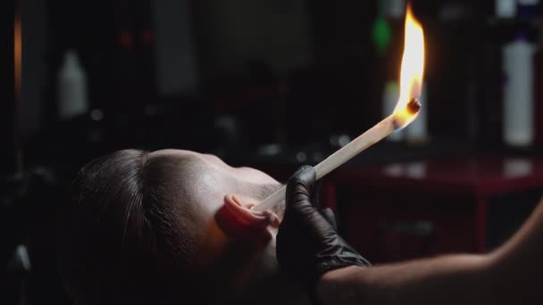 Крупный план красивого мужчины с горящей бумажной палкой в ухе — стоковое видео
