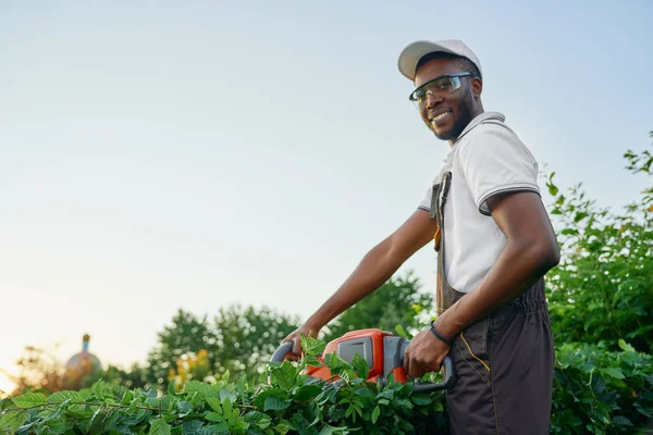 Glad afrikansk man trimma buskar med gasdrivna clipper — Stockfoto