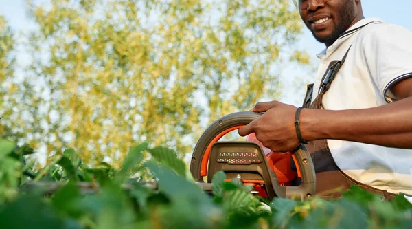 Närbild av afrikanska manliga arbetare skära buskar med trimmer — Stockfoto