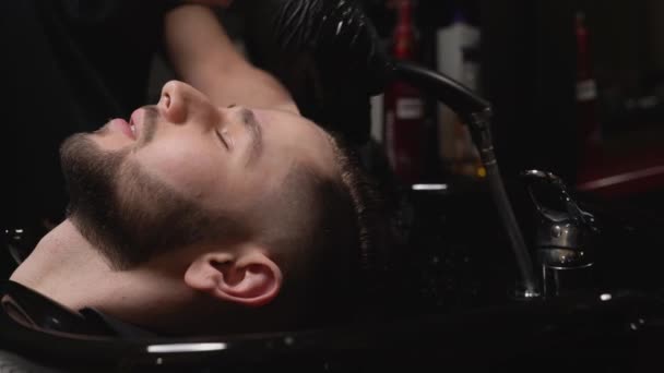 Перукар миття волосся молодого клієнта в перукарні — стокове відео