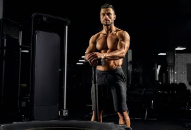 Caucasian shirtless man leaning on sledgehammer.