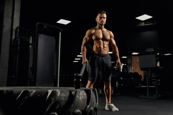 Shirtless bodybuilder holding sledgehammer in gym. — Stockfoto