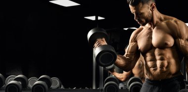 Muscular bodybuilder training biceps in gym.