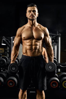 Pumped male bodybuilder holding dumbbells.
