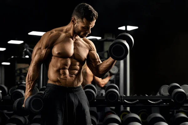 Esportista muscular construindo bíceps com halteres. — Fotografia de Stock