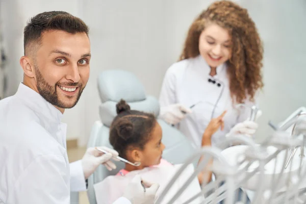 Diş hekimi ve asistanıyla dişçi koltuğunda oturan afro kız. — Stok fotoğraf