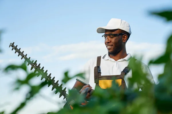 Afrikansk man i uniform arbetar i trädgården med häcksax — Stockfoto