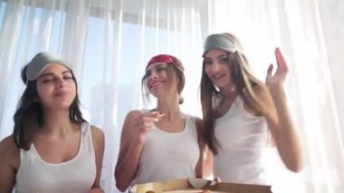 Bekarlığa veda partisinde pijamalı üç mutlu kız pizza yiyor.