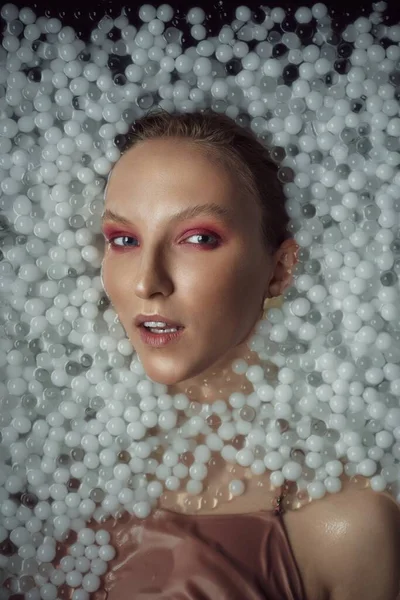 Blonde woman posing in water with balls.