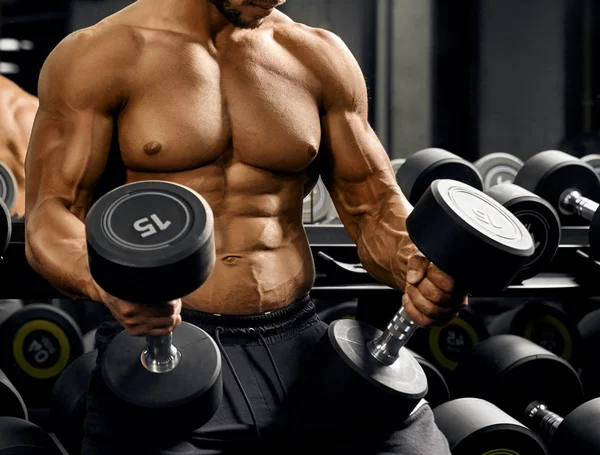 Male bodybuilder holding dumbbells on thighs. — Stock Photo, Image