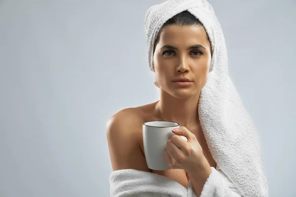 Woman in bathrobe and towel holding cup. — Stock Photo, Image